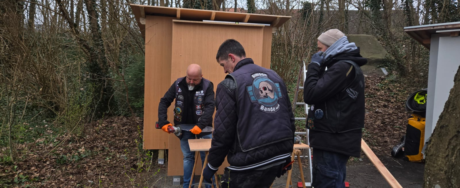 Drei Helfer bauen mit Werkzeug die Holzkonstruktion der Schutzhütte auf